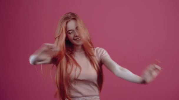 幸せな赤髪の若い女性は、踊り、彼女の手を振って、彼女の顔に笑顔で。ピンクのカジュアルなTシャツに身を包んだ20歳のハイパーティーンアー。. — ストック動画