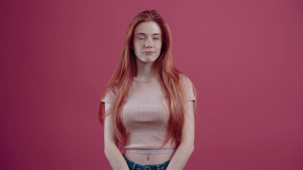 Молодая интеллигентная рыжая с улыбкой думает о новых решениях для развития. 20-летний хипстерский подросток в розовой футболке, изолированный на розовом фоне. — стоковое видео