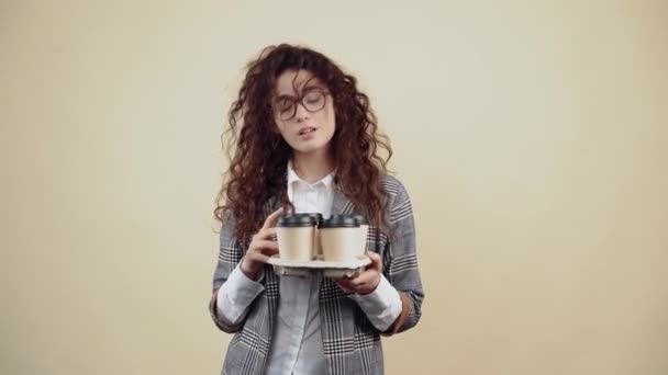 The chalky, arrogant secretary, who holds in her hand a support with 4 coffees, offers them in front. Young hipster in gray jacket and white shirt, with glasses posing isolated on beige background in — Stock Video