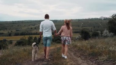 Geniş çerçeveli bir çift. Köpekleriyle yürüyorlar. Tarlada yürümeyi ve yürümeyi severler..