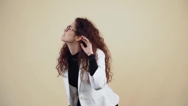 Curiosa joven con el pelo rizado, con la mano en la oreja, escuchó chismes inclinados hacia adelante. Joven hipster en chaqueta gris y camisa blanca, con gafas posando aisladas sobre fondo beige en el — Vídeo de stock