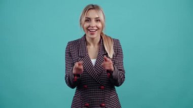 Şok olmuş genç bir kadın odaya bakıp şaşırdı ve ellerini başına koydu. Ekose ceketli güzel, olgun, genç bir sarışın. Turkuaz bir arkaplanda izole edilmiş.