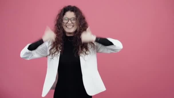 Il giovane vincitore con i capelli ricci, guarda felice con entrambe le mani il gesto come sorridere. Giovane hipster in giacca bianca e camicia nera, con occhiali in posa isolata su sfondo rosa in studio. — Video Stock