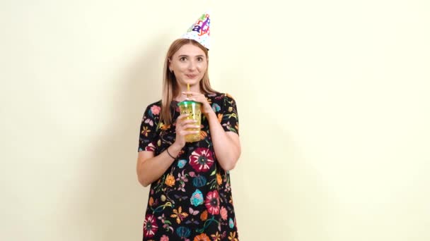 Mladá dospělá žena pije ze žluté sklenice. Mladá žena v šatech slaví své narozeniny — Stock video