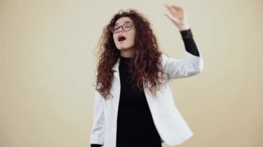Hevesli kıvırcık saçlı genç kadın el hareketlerini ve göz kırpmalarını iyi gösteriyor. Gri ceketli ve beyaz gömlekli genç hippi.,