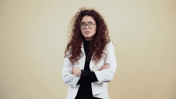 The unwell young woman with curly hair, gestures with her hands and puzzled says what, did not understand, what. Young hipster in gray jacket and white shirt, with glasses posing isolated on beige — Stock Video