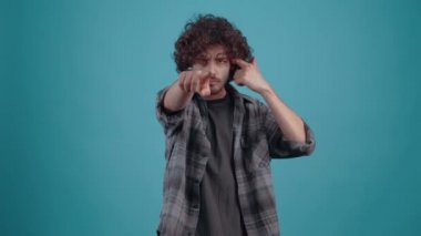 Genç sinirli hippi, parmağını yüzüne doğrultuyor ve stüdyoda turkuaz bir arka planda kötüye işaret gösteriyor. İnsanların yaşam tarzı kavramı