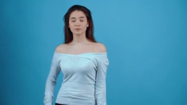 Hasta Asyalı kız hayır diyor, eli önünde, işaret parmağını hareket ettiriyor. Koyu renk saçlı, mavi bluz giymiş, stüdyoda koyu mavi bir arka planda izole edilmiş.