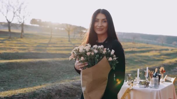 Das Porträt einer charismatischen jungen Frau in der Natur, die vor dem Hintergrund des Sonnenuntergangs einen Strauß schöner Blumen in der Hand hält. Frische junge Frau macht Heiratsantrag — Stockvideo