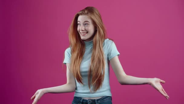 赤髪でびっくりした女の子は情報を拒否し、ピンクの背景に隔離された青いカジュアルなTシャツにジェスチャーでそれを減価償却します。人々の生活様式の概念 — ストック動画