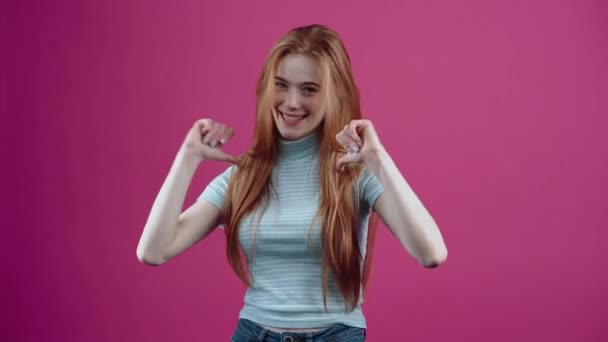 Молодая рыжая девушка демонстрирует свое хорошее настроение, показывая широкую улыбку и подобный знак, в голубой повседневной футболке, изолированной на розовом фоне. Концепция образа жизни народов — стоковое видео