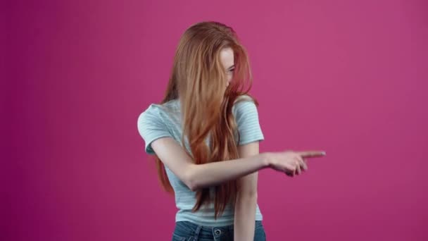 La adolescente pelirroja y optimista aprecia la elección de sus amigas a través de un gesto apreciativo, en una camiseta casual azul, aislada sobre un fondo rosa. El concepto de estilo de vida de las personas — Vídeo de stock