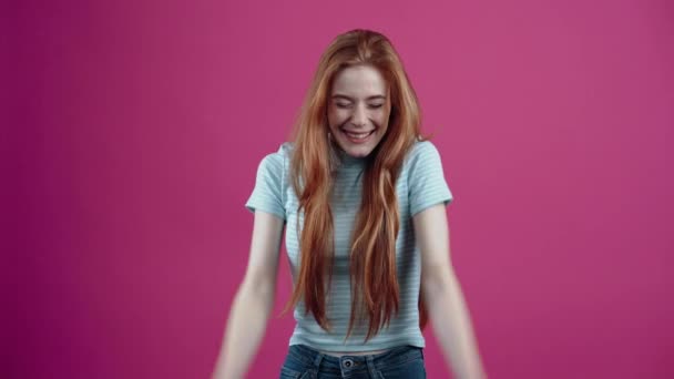 赤毛の10代の若者は、ピンクの背景に隔離された青いカジュアルなTシャツの中で、本当の勝者のように彼女の手を上げることによって彼女の結果を楽しんで幅広い笑顔を示しています。人々の生活様式の概念 — ストック動画