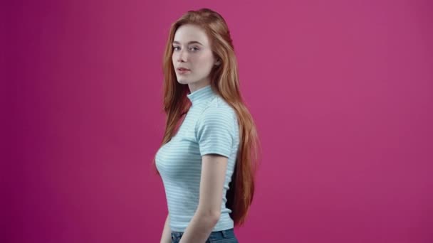 若い赤毛、興奮し、陽気な彼女の顔をして、部屋の笑顔を見て、青色のカジュアルなTシャツで、ピンクの背景に隔離された彼女の手ですごいと言う。人々の概念 — ストック動画