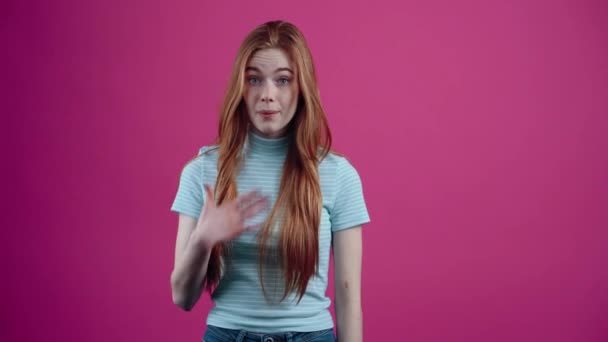 驚いた赤毛の女の子は、彼女について言われたことを否定し、彼女の頭の上の目、ピンクの背景に隔離されたカジュアルな青いTシャツを使用しています。人々の生活様式の概念 — ストック動画