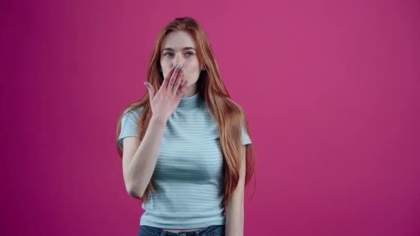 The young, optimistic redhead sends air kissing and then puts her hands on her heart as a sign of gratitude, isolated on a pink background. The concept of peoples lifestyle — Stock Video
