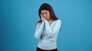 Genç esmer, çaresiz, utangaç bir şekilde gözlerini deviriyor ve ellerini göğsüne koyup dua şeklinde af diliyor. Koyu saçlı, mavi bluz giymiş, koyu tenli bir Asyalı.