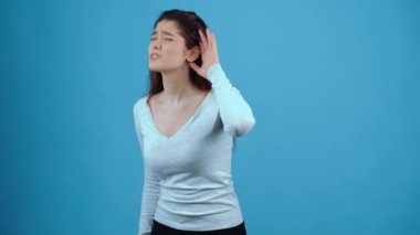 Soruyu anlamayan şüpheci kız, daha iyi duymak için elini kestanenin üzerine koyar ve eliyle soruyu tekrarlamasını ister. Koyu saçlı, mavi bluz giymiş bir Asyalı.