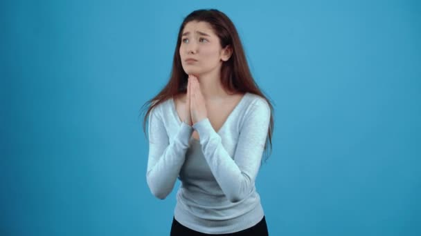 La jeune femme désespérée manifeste sa prière en montrant ses mains sous la forme d'une prière. Asiatique aux cheveux foncés, vêtu d'un chemisier bleu, isolé sur un fond bleu foncé en studio. L ' — Video