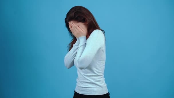 La giovane bruna, triste, piange disperatamente con il viso in mano, chiedendo finalmente aiuto con gli occhi. Asiatico con i capelli scuri, vestito con una camicetta blu, isolato su uno sfondo blu scuro nel — Video Stock