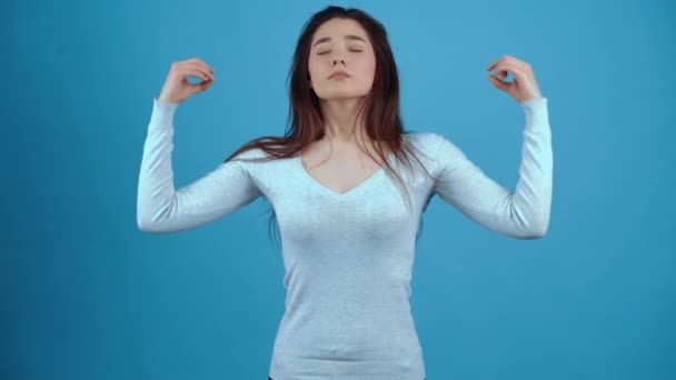 La joven morena tranquila y relajada, medita con las manos en los costados, respira con calma y luego une las manos al pecho. Asiático de pelo oscuro, vestido con una blusa azul, aislado en una oscuridad — Vídeo de stock