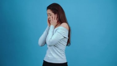 Korkmuş genç esmer, parçalara bakar ve kafası karışır, ellerini koruyucu bir kucaklamaya sokar. Koyu saçlı, mavi bluz giymiş, stüdyoda koyu mavi bir arka planda izole edilmiş.