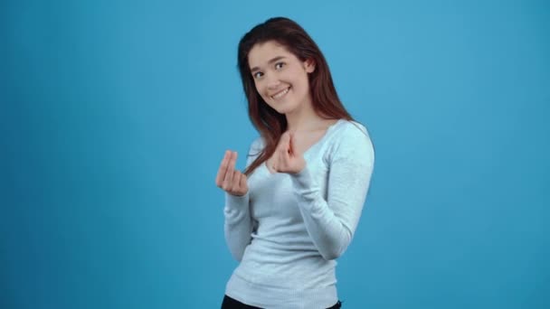 A jovem morena carismática parece chique e pede seu dinheiro através de gestos repetidos de esfregar os dedos. Asiático com cabelo escuro, vestido com uma blusa azul, isolado em um fundo azul escuro no — Vídeo de Stock