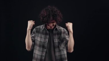 Charismatic young man surprised, points with his index fingers to one side, and then raises his hands as a winner and approves cheerfully by displaying the like sign with his thumb up. Isolated on