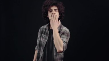 The charismatic, handsome young man transmits air kisses, after which he looks forward gracefully and hides his shameful gaze. Isolated on black background, Concept of life. Peoples emotions. 4k