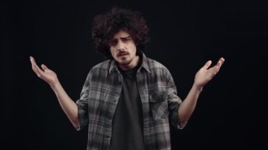 The charismatic, confused young man does not understand the question, says what and puts his hands on his head simulating a mental explosion. Isolated on black background, Concept of life. Peoples