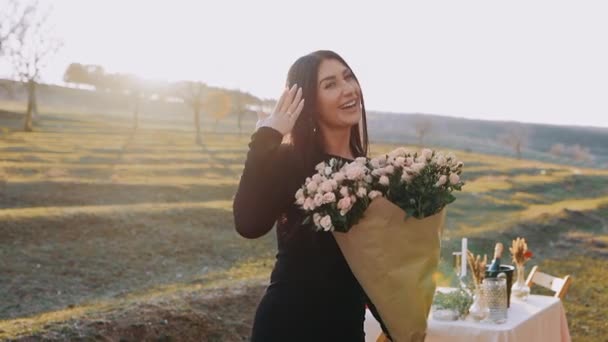Das Porträt einer charismatischen jungen Frau in der Natur, die vor dem Hintergrund des Sonnenuntergangs einen Strauß schöner Blumen in der Hand hält. Frische junge Frau macht Heiratsantrag — Stockvideo
