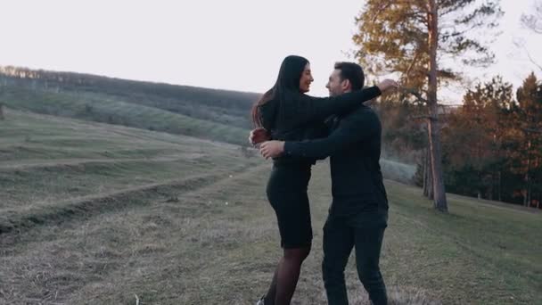 Unga par förälskade i naturen håller händer och ler, i slutet kramar den unge mannen sin flickvän och lyfter henne i sina armar, — Stockvideo