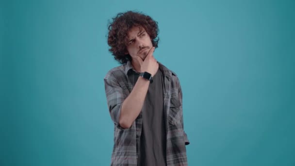 The young, curly-haired hipster thinks, looking to the right with his hand on his chin. Isolated on black background, Concept of life. Peoples emotions. 4k portrait — Stok video