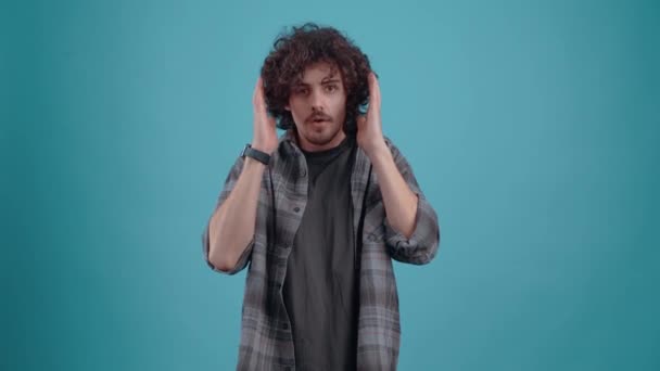 The young, curly-haired hipster hears news that shocks him and shouts wow with his hands on his head. Isolated on black background, Concept of life. Peoples emotions. 4k portrait — Vídeo de stock