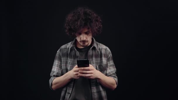 The charismatic young man, seriously, looks on the phone, after which he receives a message that makes him very happy and restores his good mood. Isolated on black background, Concept of life. People — Stock videók