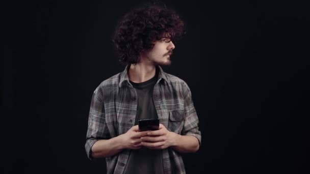 The charismatic young man, focused, looks on the phone, after which an event distracts him, and he shows his amazement, saying wow. Isolated on black background, Concept of life. Peoples emotions. 4k — Αρχείο Βίντεο