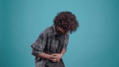 The grieving young man clings to his stomach, feels an acute pain that makes him close his eyes and hunch. Isolated on black background, Concept of life. Peoples emotions. 4k portrait