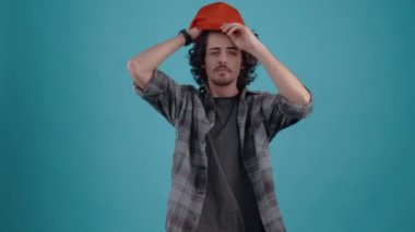 The charismatic young man puts his cap on his head, arranges his hair and gives confident eyebrows. Isolated on black background, Concept of life. Peoples emotions. 4k portrait