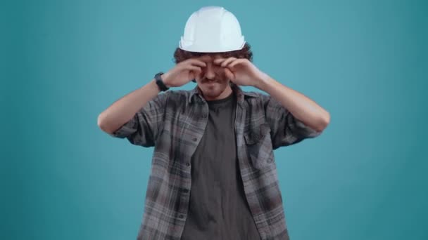 Харизматичный молодой человек с гордостью надевает шлем инженера на голову, обеспечивает ее безопасность, ударяя ее и показывая знак "как". изолированы на черном фоне, концепция жизни. peoples — стоковое видео