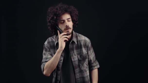 The charismatic young man talks on the phone, astonished, raises his eyebrows, receives wonderful news that makes him raise his arm in a winning way. Isolated on black background, Concept of life — Vídeo de Stock