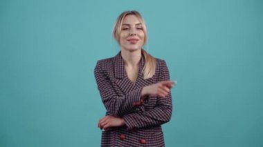 The optimistic blonde slowly raises her index finger to one side and displays a wide smile and amused by the situation.Isolated on a turquoise background. The concept of life. Peoples emotions. 4k