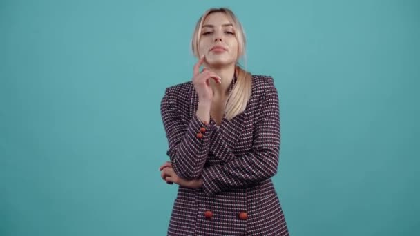 The charismatic blonde dreamily puts her hand to her chin and looks confidently to one side. Isolated on a turquoise background.The concept of life. Peoples emotions. 4k portrait — Vídeo de stock