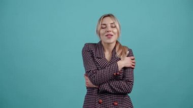 The portrait of a dreamy young woman who cleverly crosses her hands on her chest, plays with her hair and flirts with her eyes, displays a wide smile.Isolated on a turquoise background. The concept of
