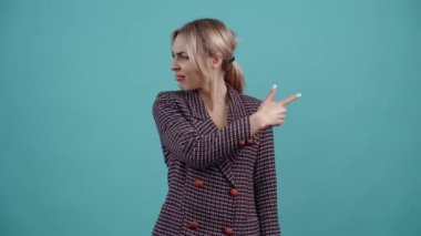 The charismatic young woman suddenly turns her head and index finger in opposite directions, shows her friend something shocking, looks subtle.Isolated on a turquoise background. The concept of life