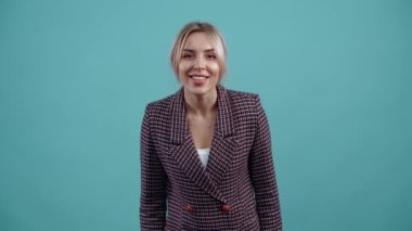 The beautiful blonde looks focused ahead, with her hands clasped to her chest, hears a compliment that excites her, displays a wide smile. Isolated on a turquoise background.The concept of life