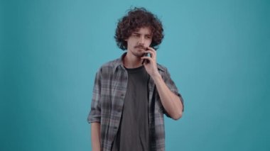 The charismatic young man receives a call, is told news that delights him, then raises his winning arm. Isolated on a turquoise background. Concept of life. Peoples emotions. 4k portrait