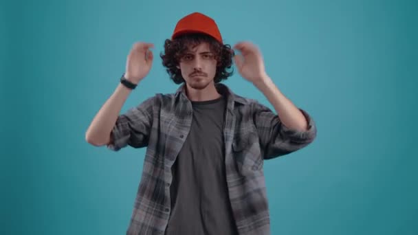 The charismatic young man, energetically puts his cap on his head, looks questioningly forward and then angrily jumps up and breathes his sleeve. isolated over turquoise background.Concept of life — Stockvideo