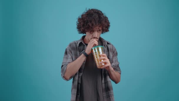 The young chalk thirstily drinks juice from the glass, with the straw, after which he puts his hand on his belly, satisfied. Isolated on a turquoise background. Concept of life. Peoples emotions. 4k — Vídeo de stock