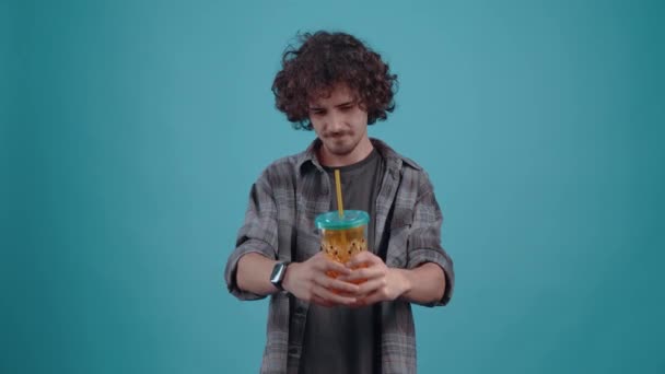 The charismatic boy spreads his glass of juice and convinces his friend to try because it is tasty. Isolated on a turquoise background. Concept of life. Peoples emotions. 4k portrait — Αρχείο Βίντεο