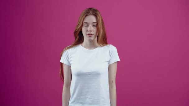 Are you ready. The shy and beautiful redhead looks embarrassingly with both index fingers in front and then displays a wide smile. Freckled teenage girl in a white T-shirt, isolated on a pink — Stock Video